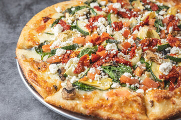 Close up of Mediterranean style pizza on a pizza platter indoors on a gray table