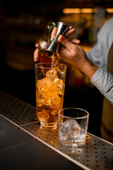 hand of the bartender gently pours beverage from jigger into mixing cup with ice