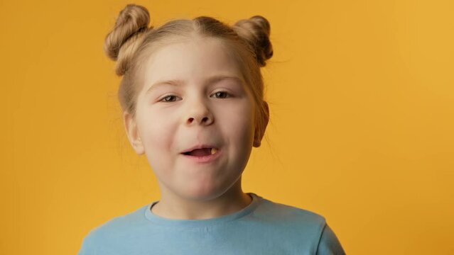 Little girl eating candy on yellow background. Cute toothless girl tasting sweet candy. Close-up in 4K, UHD