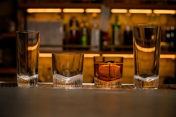 front view of a group of empty and one full cocktail glasses on the bar counter.