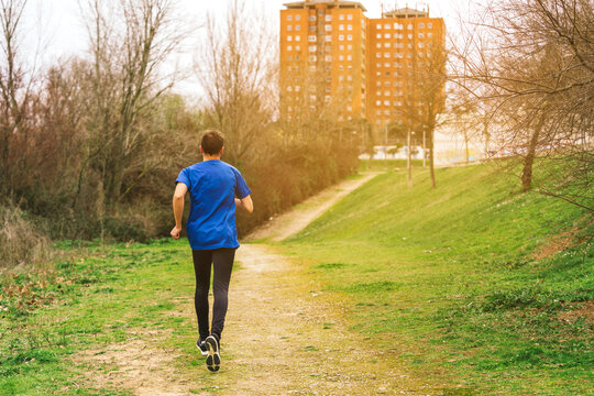 A Young Caucasian Spanish Man Running With His Back To The Camera In A Park At Sunrise.