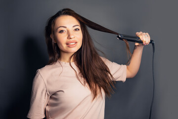 Portrait of charming girl using straightener for curly hair making styling isolated over white background preparing for party. Wellbeing wellness pampering concept