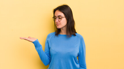 young hispanic woman feeling happy and smiling casually, looking to an object or concept held on...