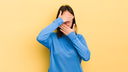 young hispanic woman covering face with both hands saying no to the camera! refusing pictures or...