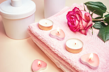 Fototapeta na wymiar Burning candles and rose on pink and white towels. Accessories for spa treatments in the salon, hotel. Focus concept. Bluering.