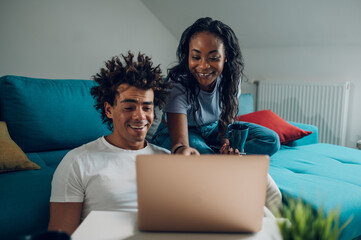 African american couple relaxing on couch with laptop and coffee at home