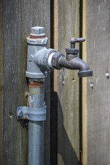 Outdoor faucet spigot for hose hook-up to water plants and gardens in yard against wood background.