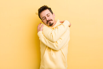 young hispanic man feeling in love, smiling, cuddling and hugging self, staying single, being...