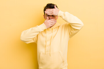 young hispanic man covering face with both hands saying no to the camera! refusing pictures or...