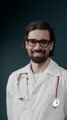 Smiling young medical doctor in glasses and with statoscope wearing white coat in a green room