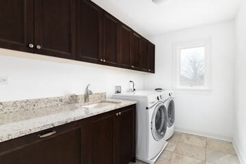 A laundry room with white washer and dryer appliances, dark mahogany wood cabinets, and granite countertop.