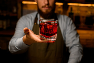 great front view of glass with bright drink which hand of a male bartender gently holds