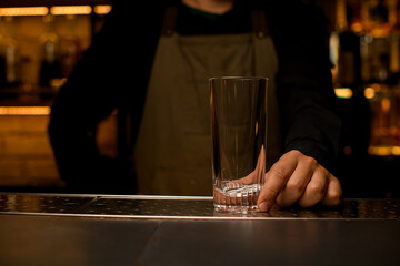 front view of clean transparent empty cocktail glass on bar counter which male hand holds