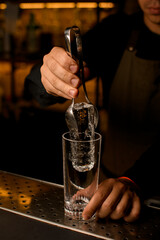 hand of bartender holds a piece of ice with tongs and accurate puts it into glass