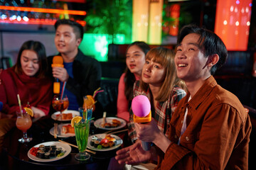Asian friends singing into microphone at karaoke party at club