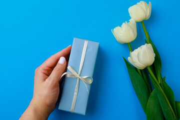 Womans hand holding Gift box .Spring flowers on color background. Happy womens day. Happy Mothers day.Hello Spring- Image