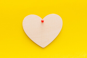 wooden heart on a yellow background pinned with a button