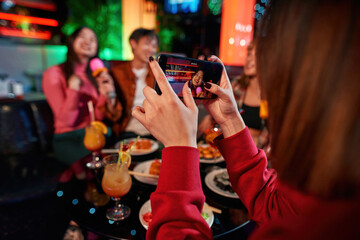 Asian girl taking photo her friends at karaoke party in bar