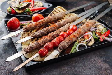 Traditional Turk Adana kebap on shashlik skewer with barbecue vegetable and flatbread served as close-up on a rustic metal tray