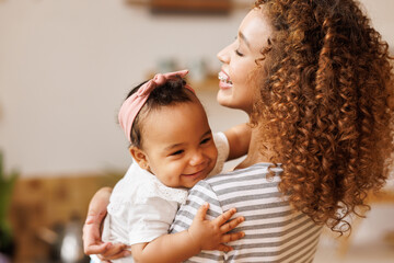 Happy, cheerful ethnic mom holds a laughing baby daughter in her arms.