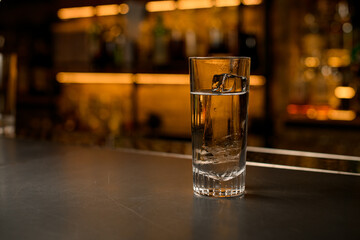 front view of transparent cocktail glass with ice cube and tonic on bar counter