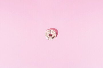 Small donuts with white glaze in various colors with colorful crumbs on a pink pastel background. Minimal design and pattern.