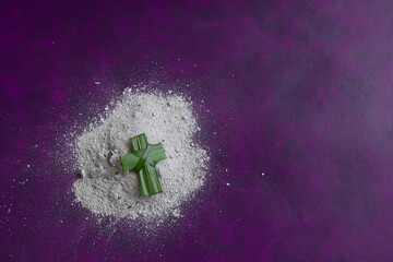 Green palm cross on a pile of ashes on a dark purple background with copy space - obrazy, fototapety, plakaty
