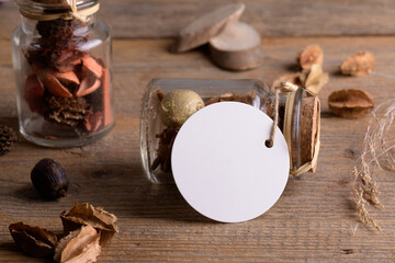 Round white tag mockup on glass jar with dry perfume a wooden background with boho decoration, element for packing