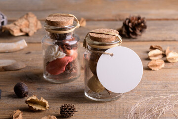 Round white tag mockup on glass jars with dry perfume a wooden background with boho decoration, element for packing. Label product mockup and natural eco design. Bohemian wedding gift, wedding favors