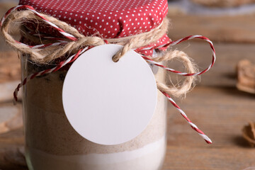 Round white gift tag mockup on a jar with mixture of ingredients for baking cookies for Christmas...
