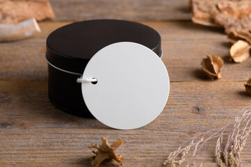 Round white gift tag mockup on black round box on rustic wooden background with boho decoration....