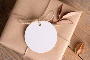 Round white gift tag mockup on craft wrapped presents on rustic wooden background with boho decoration