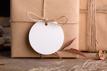 Round white gift tag mockup on Christmas or Valentines Day wrapped presents on rustic wooden...