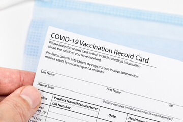 Obraz premium Womans hand holds coronavirus vaccination record card on background blue medical mask. Concept of defeating Covid-19 - Image