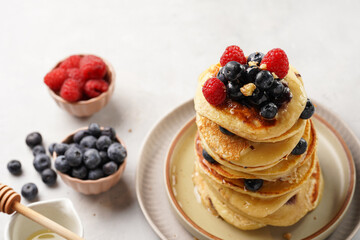 Fitness blueberry pancakes with protein, raspberries and walnuts stacked on top of each other on light grey background