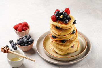 Fitness blueberry pancakes with protein, raspberries and walnuts stacked on top of each other on light grey background