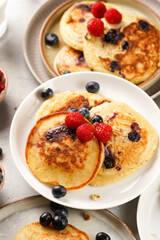 Fitness blueberry pancakes with protein, raspberries and walnuts on several white plates on light grey background