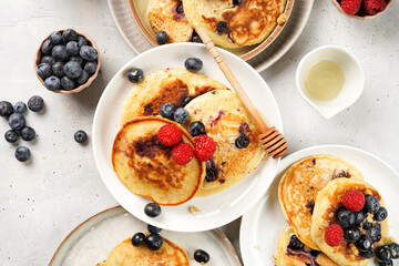 Fitness blueberry pancakes with protein, raspberries and walnuts on several white plates on light grey background