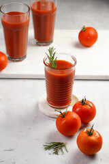 Several glasses full with red non-alcoholic tomato juice on marble plate on light grey background