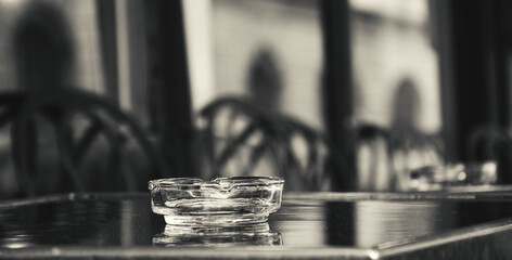 Terrace of a cafe with empty glass ashtray on a table. Paris, France. Smoking addiction health issue. Black white historic photo.