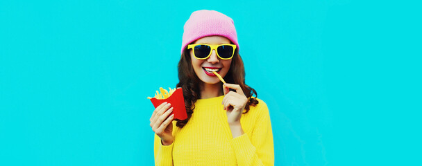 Portrait of stylish happy smiling young woman eating french fries fast food on blue colorful...