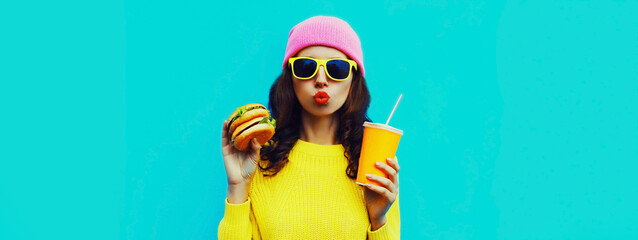 Portrait of stylish young woman with burger and cup of juice fast food on blue colorful background