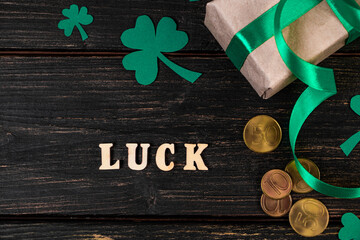 Concept for St. Patrick's Day. The word luck, clover shamrock and gift with a green ribbon on a dark wooden background.