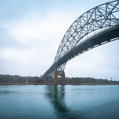 Fototapeta premium Arching steel bridge over the water. Bourne Bridge and Cape Cod Canal in a foggy rainy morning.