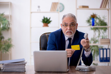 Old male employee holding credit card in the office