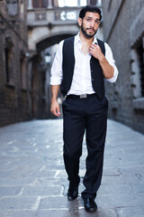 Portrait of handsome man in formalwear walking along ancient street.