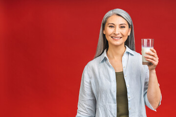 Asian senior mature aged woman drinking milk for calcium food and healthy lifestyle concept isolated on red background.