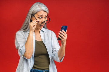 Photo portrait of asian shocked amazed surprised senior aged mature woman holding mobile phone seeing crazy discounts wearing casual isolated on red background. - 488887946