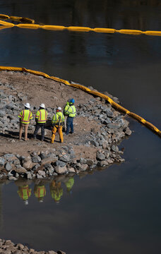 Construction Workers at Bridge Work Site on River With Oil Booms and Reflection in Water
