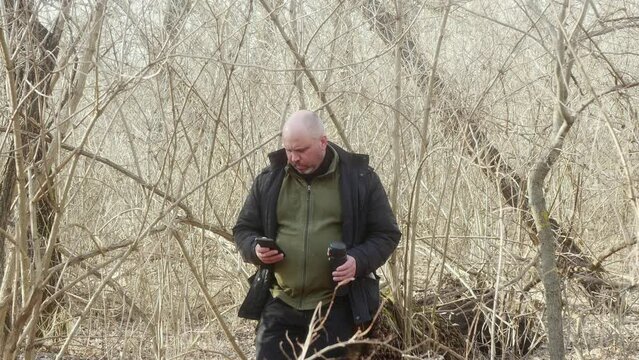 a man in a dense forest near a large stump looks into his mobile phone